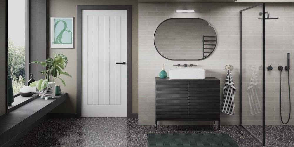 Bathroom with a black vanity holding a white sink, situated beneath an oval mirror. Nearby, a glass shower enclosure. Top skylight brightens the space. Decorative plants and framed art on left windowsill.